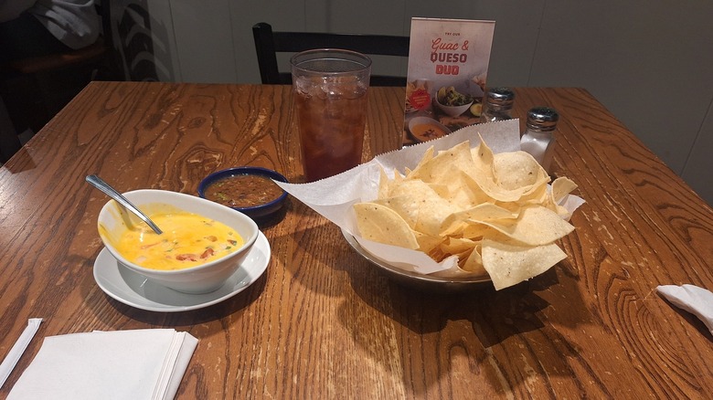 A bowl of On the Border chips with salsa and queso on a wooden table