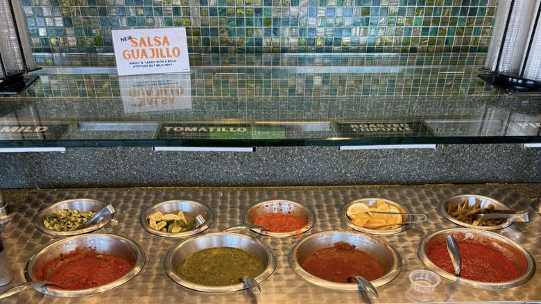 A tiled restaurant salsa bar with four selections and additional condiments
