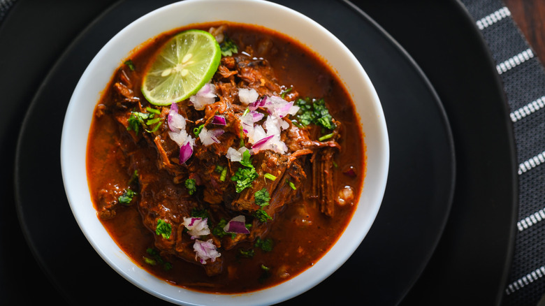 Mexican beef stew garnished with onion, cilantro, and lime on black plate