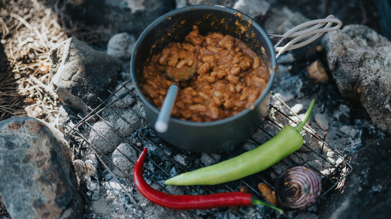 Pot of beans on top of a coal fire pit with peppers and onions beside it