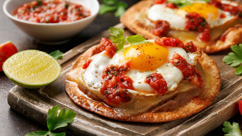 Tortilla topped with fried egg and salsa on wooden board with lime