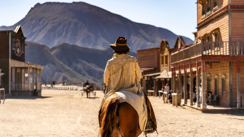 Theme park scene with cowboy on horse staring at Old West town and mountain landscape