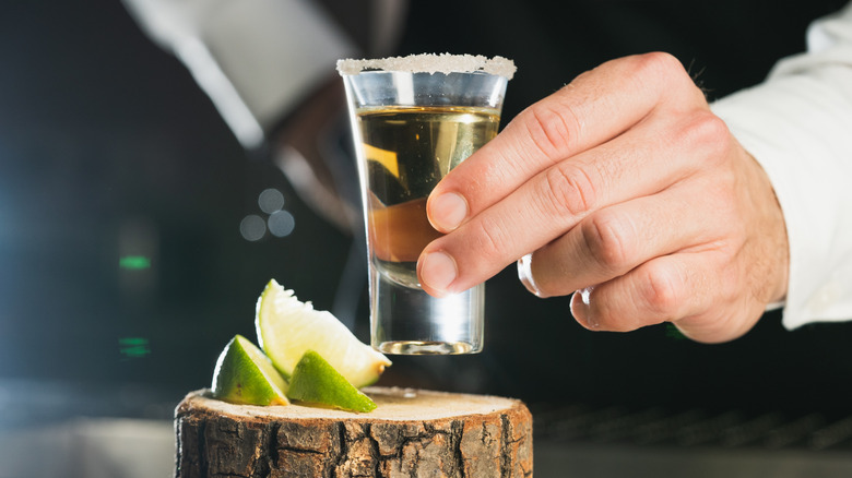 Bartender placing rimmed tequila shot next to lime slices on wooden coaster.