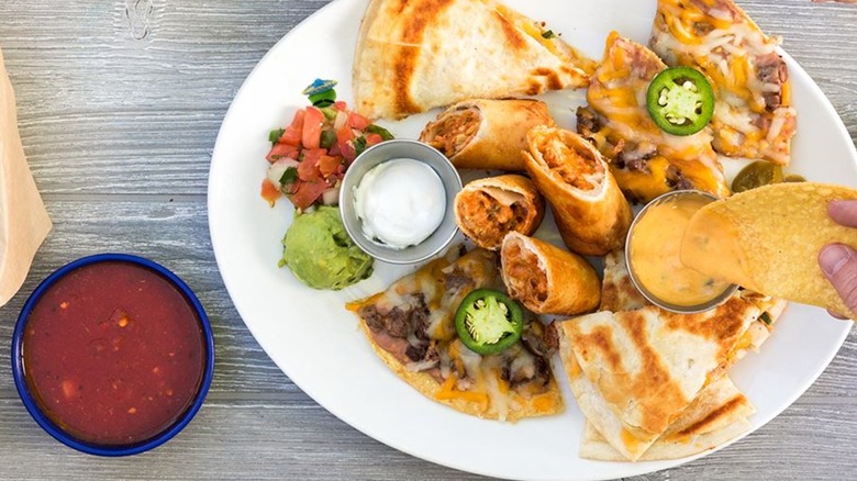 Salsa next to a plate of quesadillas, fajita nachos, and chicken flautas from On The Border