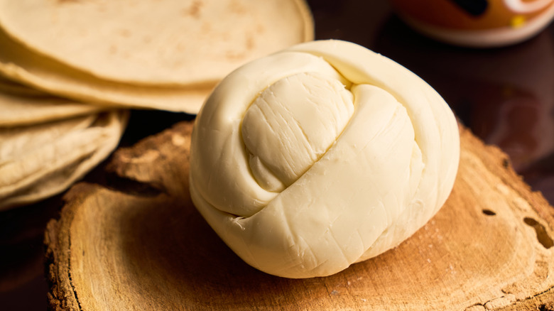 Queso Oaxaca in a knot-like shape on a wooden board with tortillas in the background