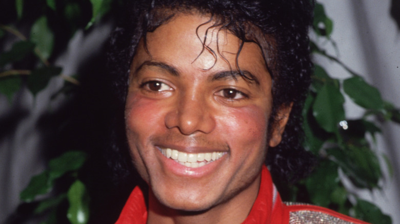 Michael Jackson smiling and wearing red leather jacket in front of a potted plant