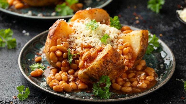 A jacket or baked potato with beans, cheese, and herbs on a plate.