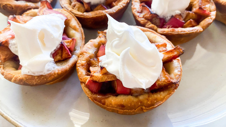 mini apple pies with whipped cream topping on white plate