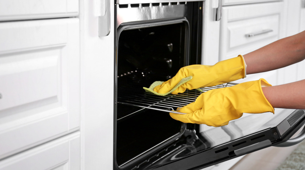 Hands wearing rubber gloves while cleaning an oven