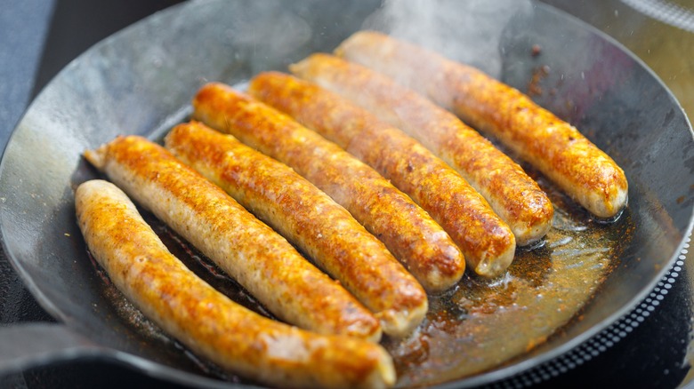 Browning steaming sausages in pan