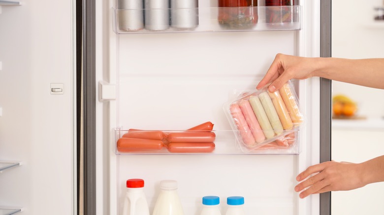Hand grabbing sausages from fridge door