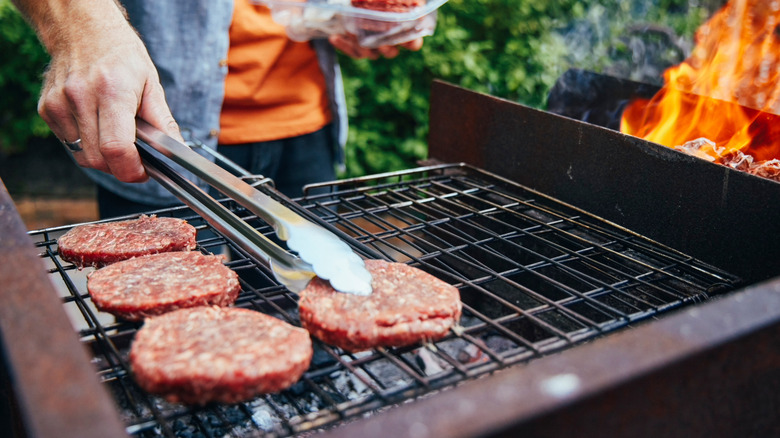 man with tongs grilling burger patties