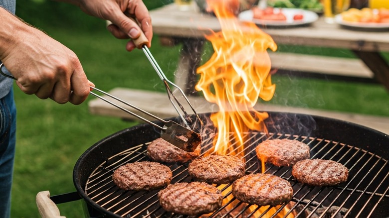 hands tending to flaming grilled burgers