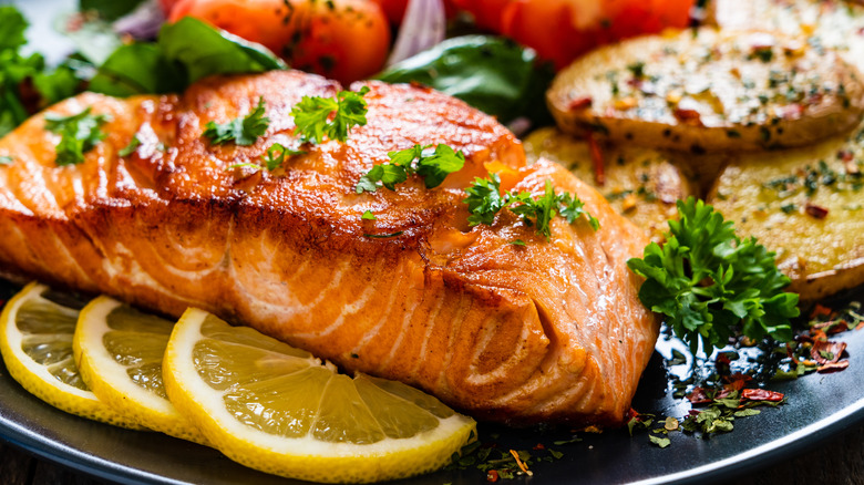 Fried salmon steak with potatoes and vegetables on wooden table