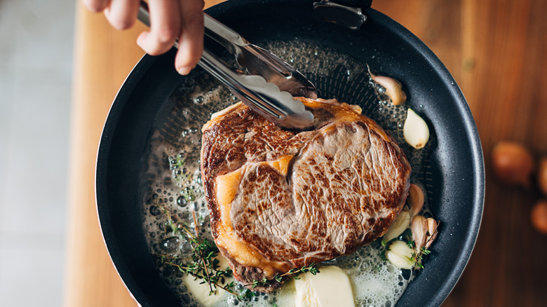 person searing meat in a frying pan