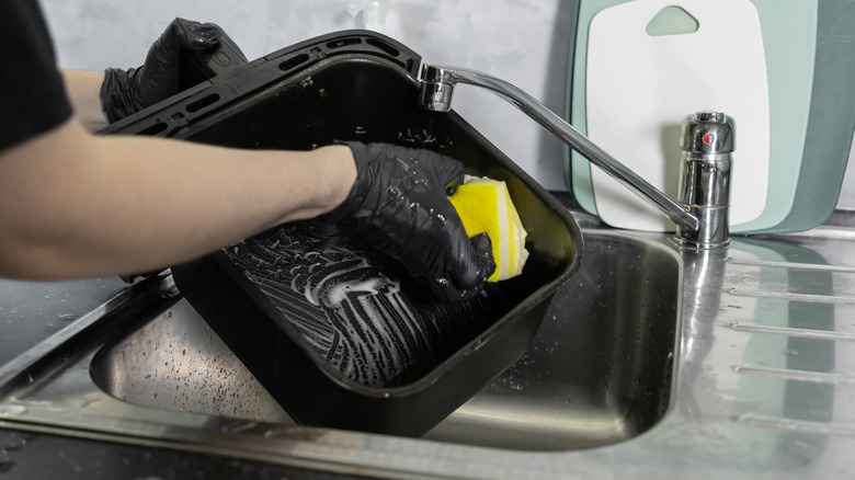 Hands wearing gloves scrubbing an air fryer basket