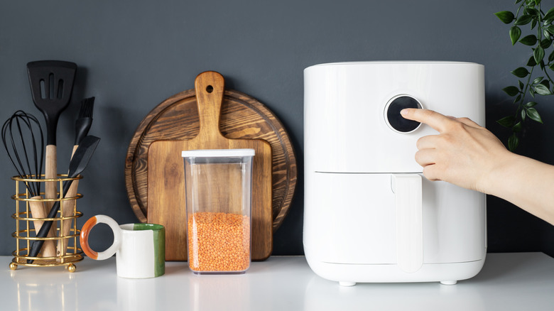 Hand pressing button on air fryer on counter with cutting boards and utensils