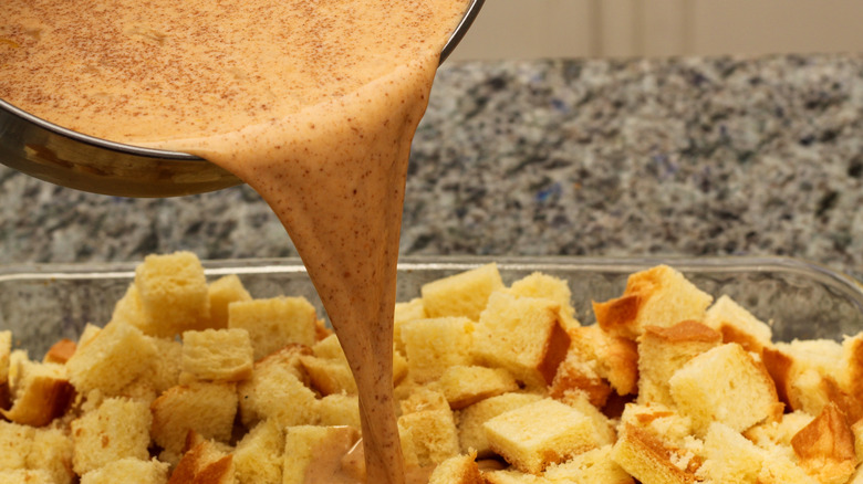 Custard being poured onto cubed bread