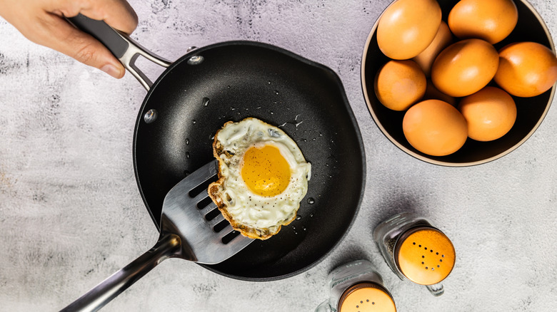 person using metal utensil to cook egg on nonstick pan