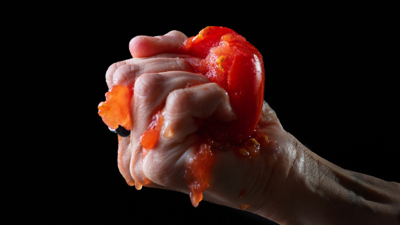Hand squeezing whole tomato