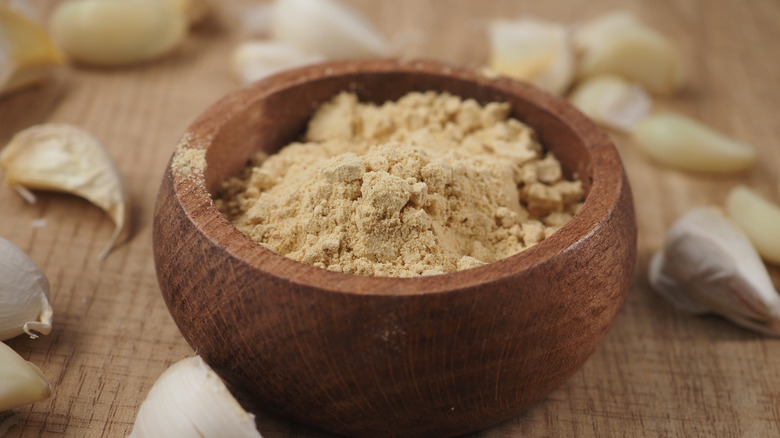 Bowl of garlic powder surrounded by fresh garlic cloves