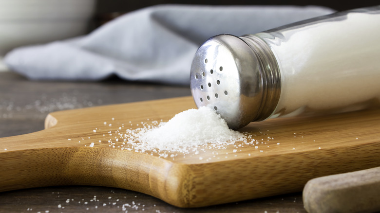 Salt spilled from salt shaker onto wooden cutting board