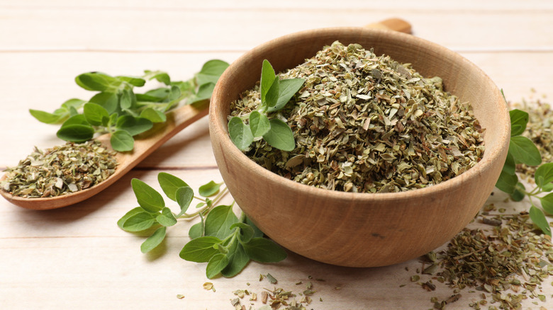 Bowl of dried oregano alongside fresh oregano leaves