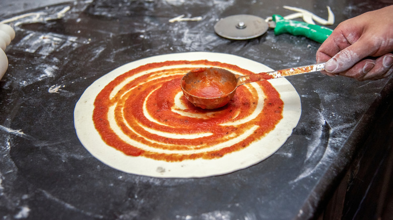 Pizza sauce being spread on dough