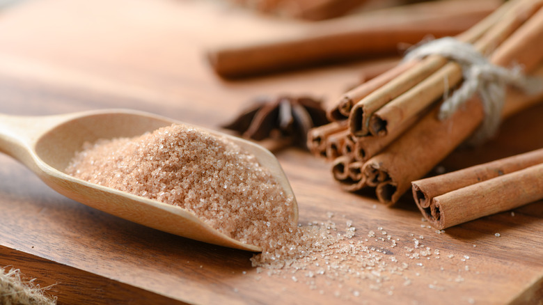 Scoop of cinnamon sugar on wooden board with cinnamon sticks in background