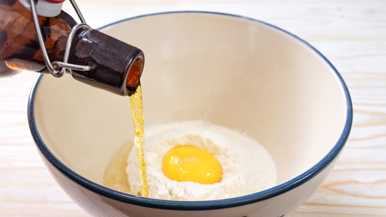 Beer pouring into ceramic bowl containing egg and flour