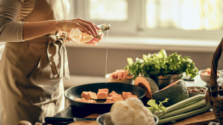 Cook drizzling pan of pumpkin with oil on kitchen counter laden with ingredients