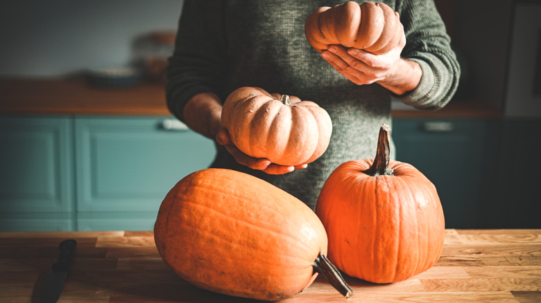 Two pumpkins on the counter, with person standing behind holding two smaller pumpkins