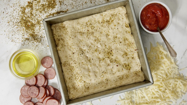 Detroit pizza dough in pan surrounded by ingredients