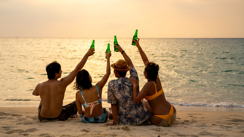 Group of friends on the beach, raising bottles of beer