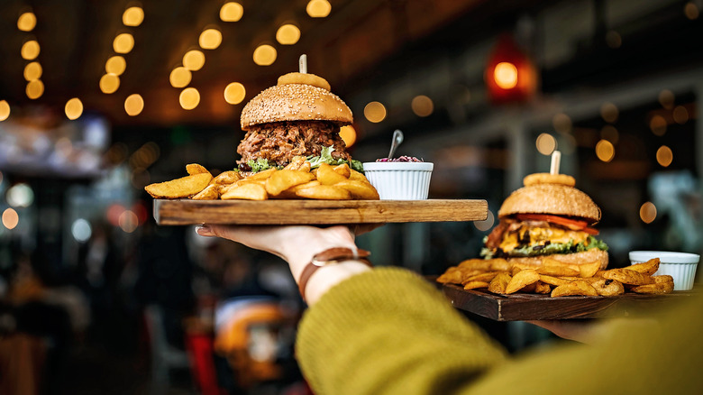 holding boards with burgers and fries in restaurant