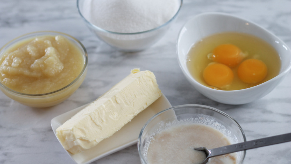 ciotole di uova, zucchero, salsa di mele e latticello, insieme a un panetto di burro su un bancone di marmo grigio e bianco