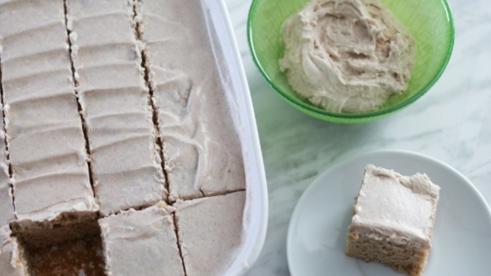 applesauce cake in a white cake pan with a slice on a white plate and frosting in a green bowl