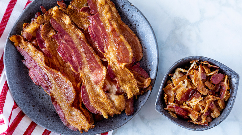 Slices of cooked bacon next to dish of crumbled bacon