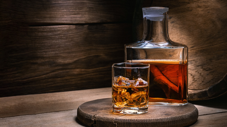 Bottle and glass of whiskey on a wooden board in front of a barrel