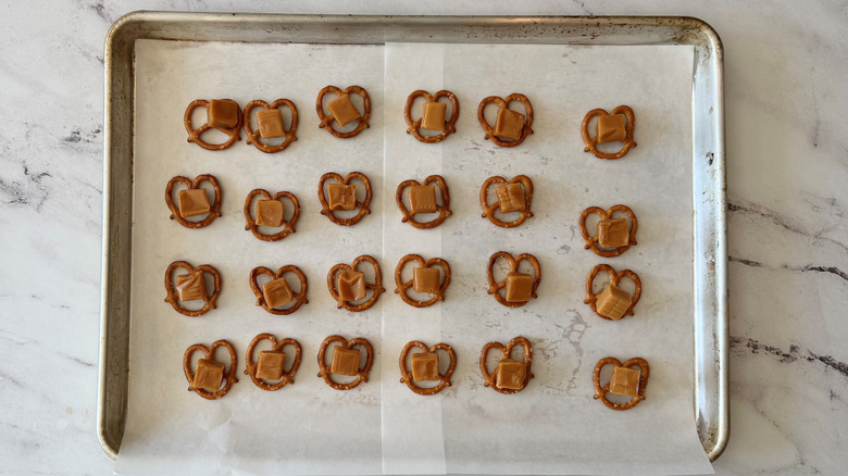 Pretzels topped with caramel squares on baking sheet