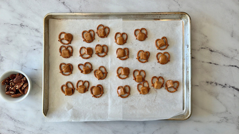 Pretzels topped with caramel squares on baking sheet