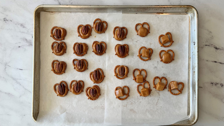Pretzels on baking sheet topped with caramels and pecans