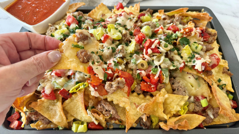 Hand pulling chip off platter of Italian nachos