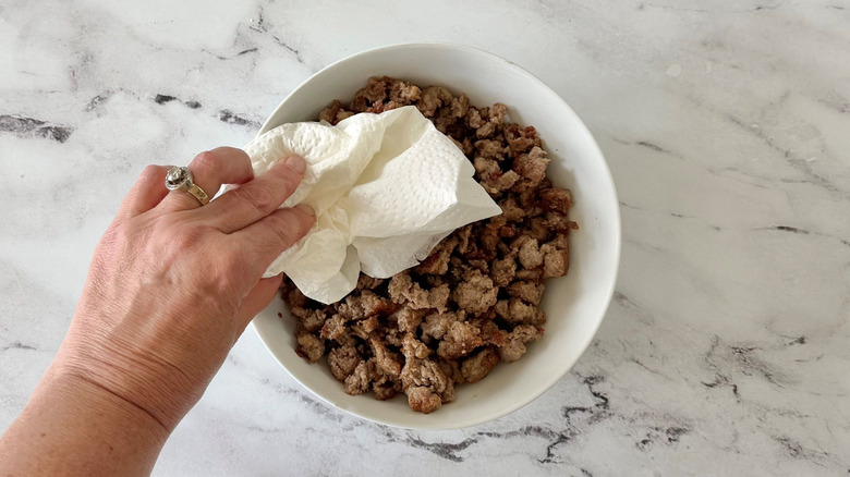 Hand patting bowl of Italian sausage with paper towels