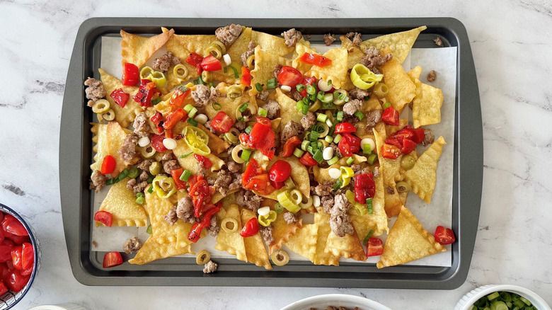 Italian nachos with various toppings on baking sheet