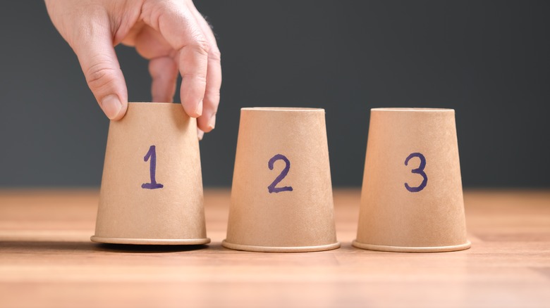 Hand with three paper cups labeled 1, 2, 3