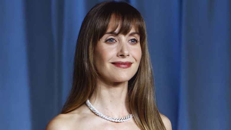 Actress Alison Brie wearing sparkling silver gown in front of blue curtain.