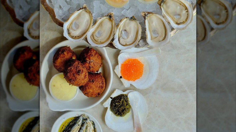 Four hush puppies with dipping sauce next to oysters on ice.