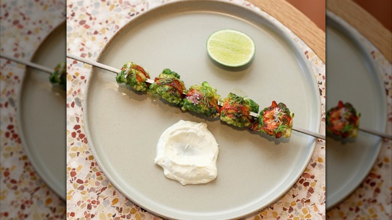 Grilled lobster skewer on gray plate with yogurt and lime.