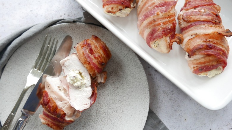 Stuffed chicken breasts wrapped with bacon placed on two different plates.